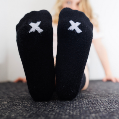 girl wearing black sensory seam free socks with white 'X' marks on a carpeted floor.
