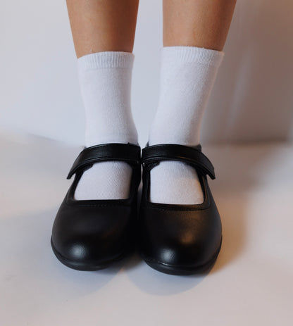 Black shoes with white sensory friendly socks on a neutral background for children with autism and ADHD.