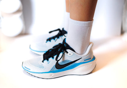 White running shoes with black and blue accents worn by a person on a light background. Wearing white sensory friendly socks.